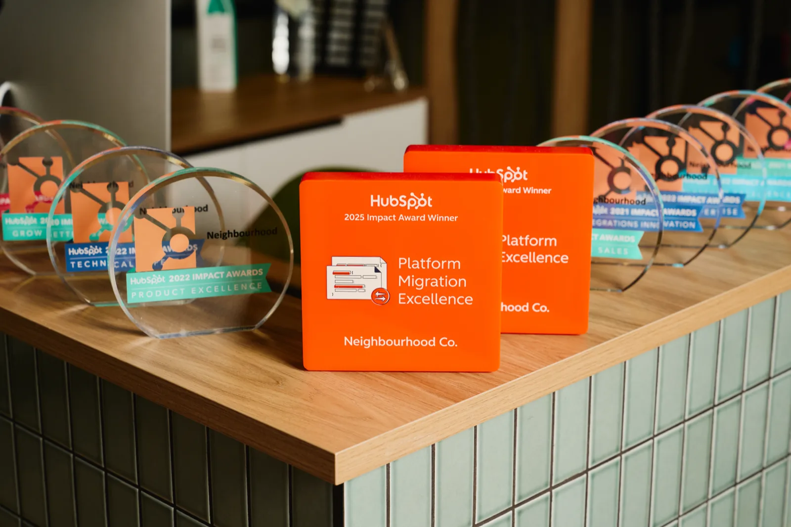 The 2025 HubSpot Impact Awards for Platform Migration Excellence and Platform Excellence, in front of the older Impact Award trophies on the office shelf