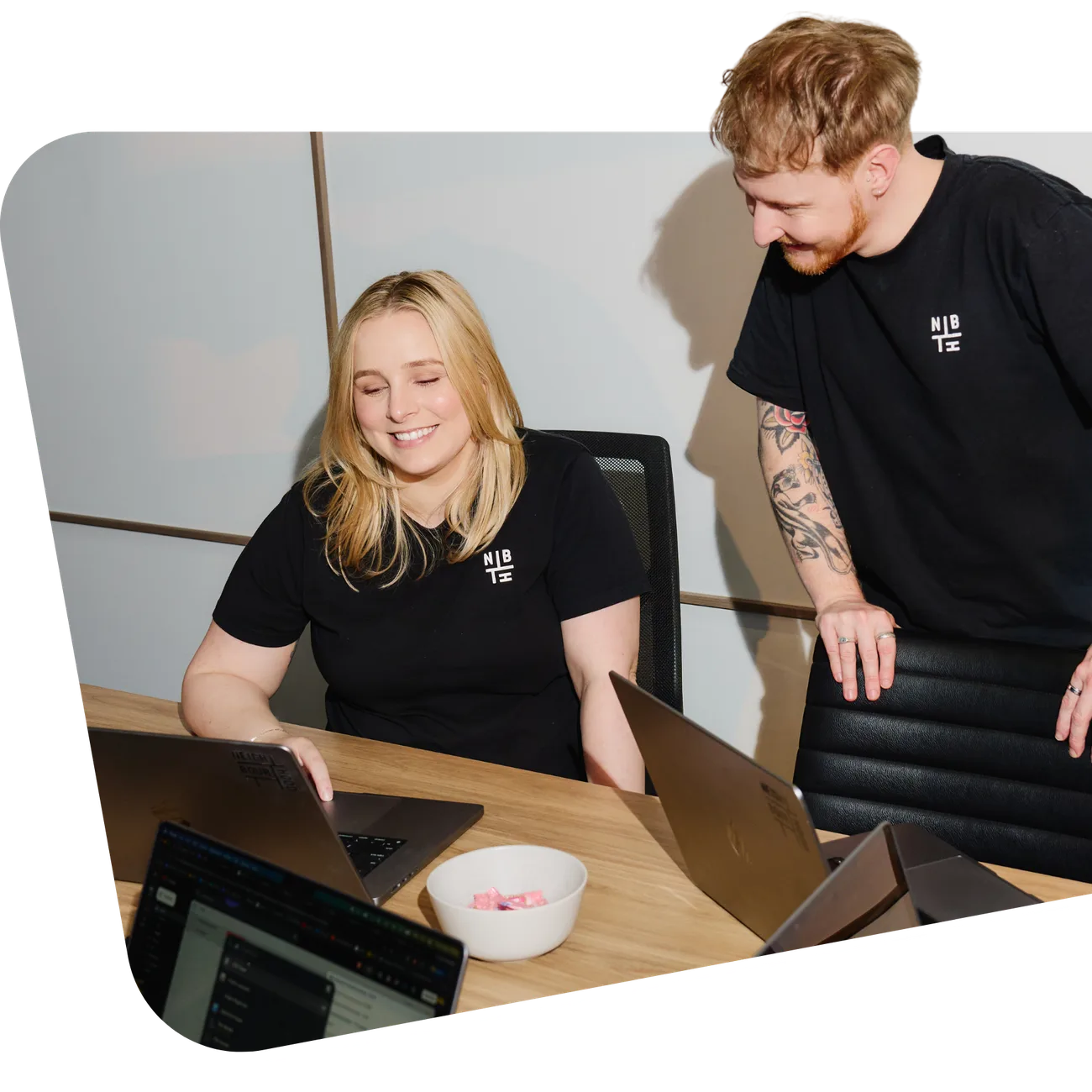 Two of the Neighbourhood team at a desk, one seated at a laptop and one leaning in, both laughing