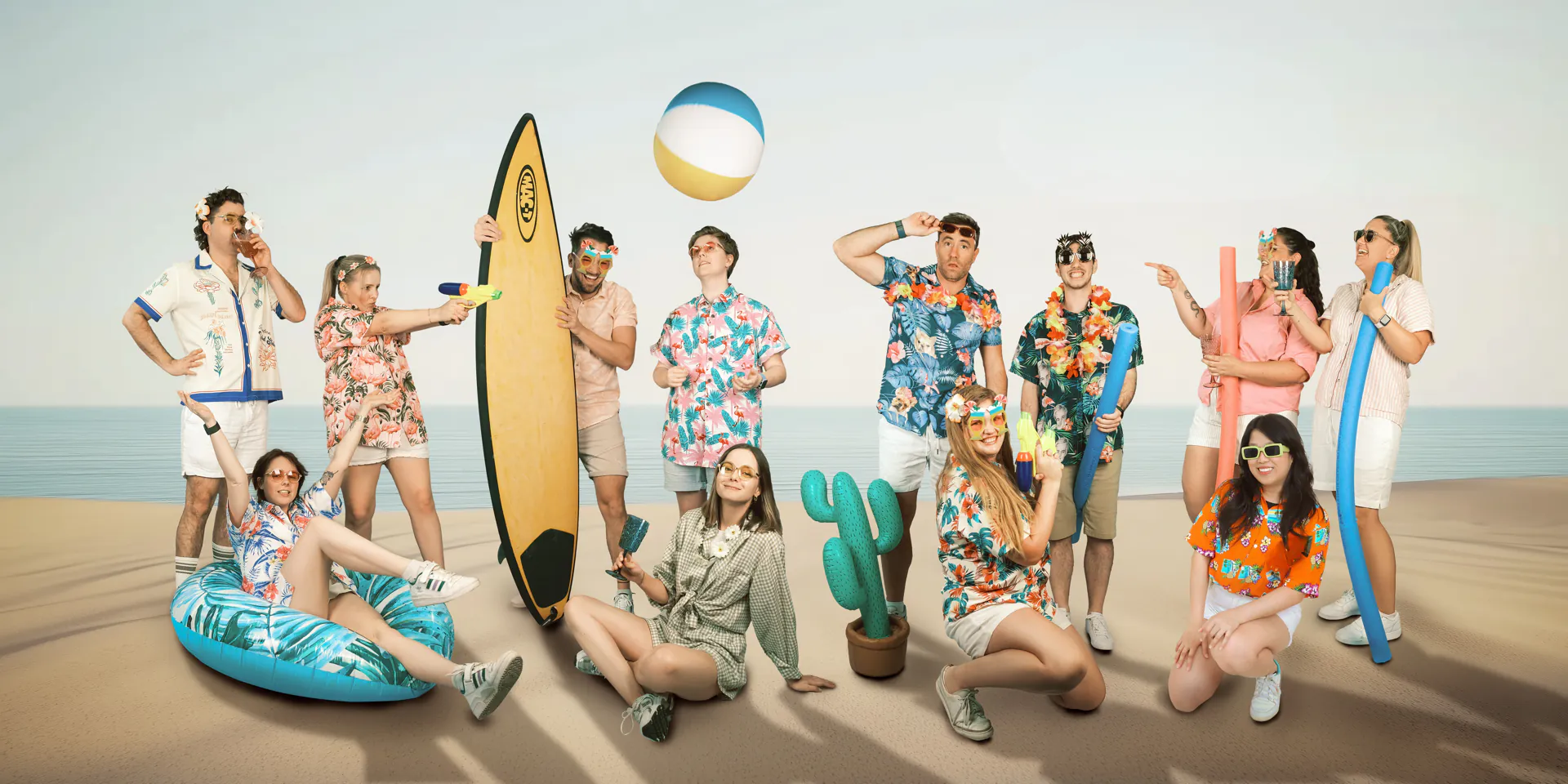 The Neighbourhood crew mucking about on the beach with surfboards, pool floats, water guns and Hawaiian shirts.
