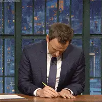 A man in a suit at a desk, scribbling meeting notes by hand