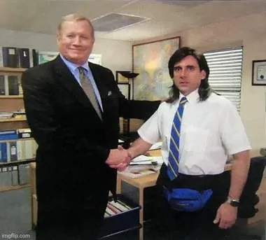 A still from The Office of two colleagues shaking hands across a desk