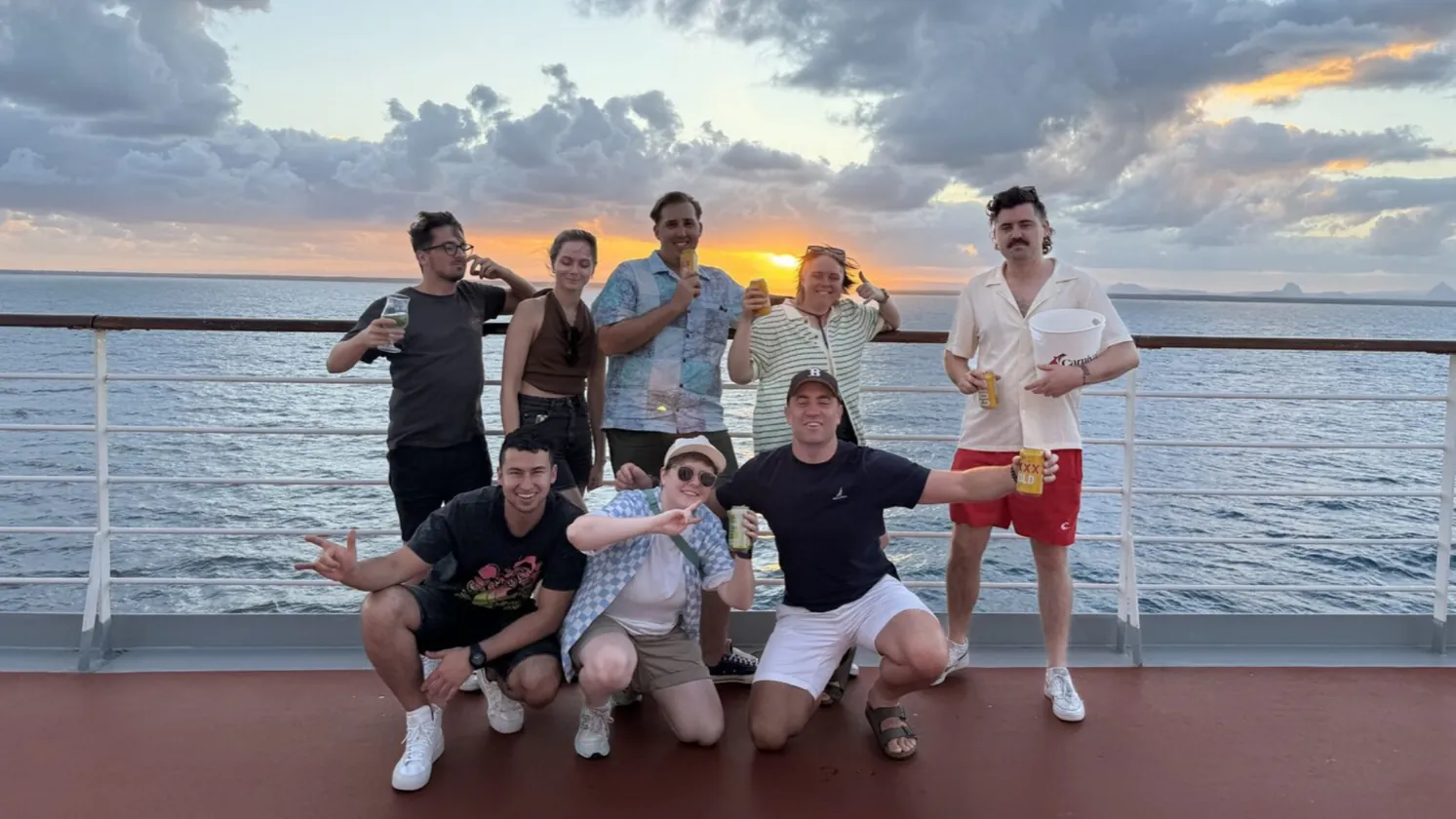 Nine of the crew on a cruise ship deck at sunset with the Glass House Mountains behind