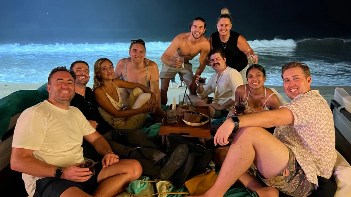 The crew sitting on beanbags on the sand at night with the surf behind them