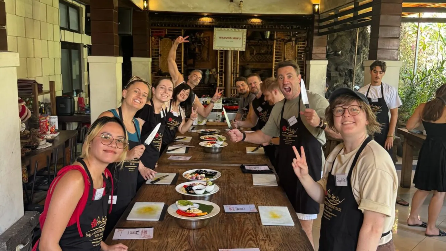 The crew around the long table at the Balinese cooking class, knives up