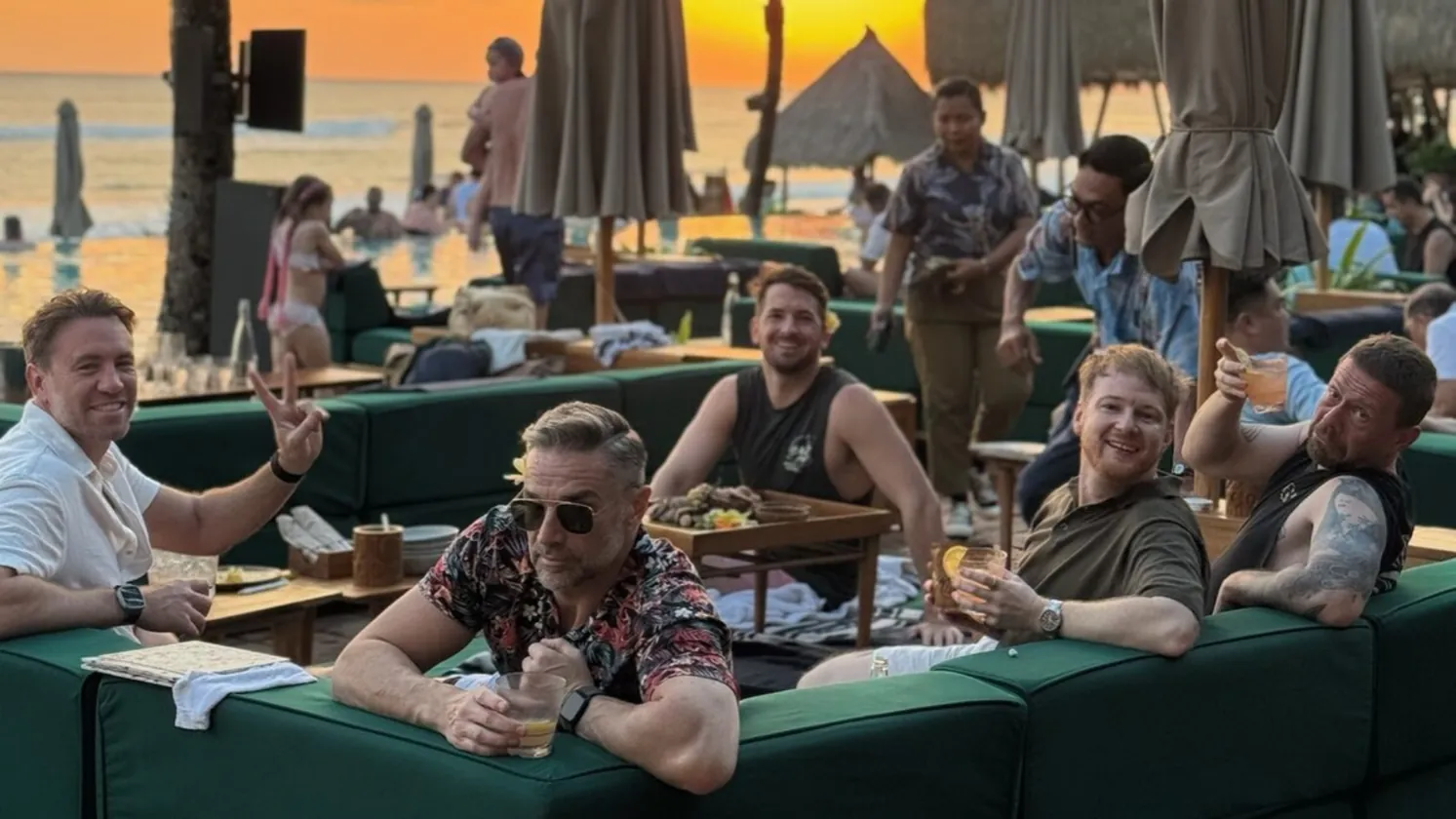Six of the crew on green lounges at a Bali beach club as the sun goes down