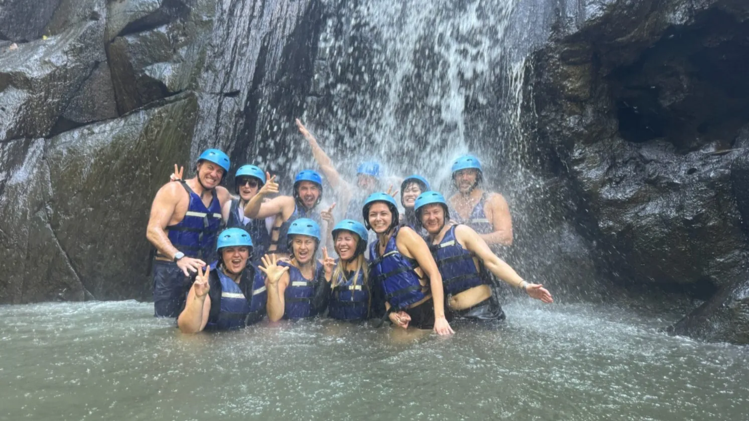 The crew in helmets and life jackets standing under a waterfall in Bali