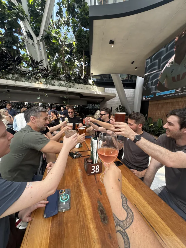 The team reaching across a long table to clink glasses at a team lunch