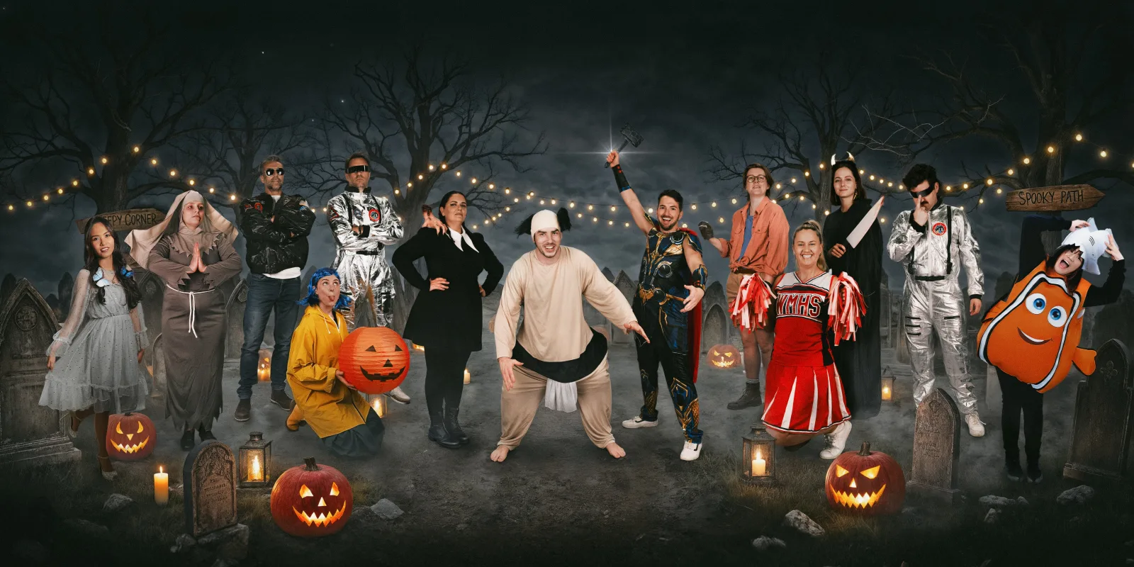 The Neighbourhood crew in full Halloween costume on a dark set with carved pumpkins and string lights