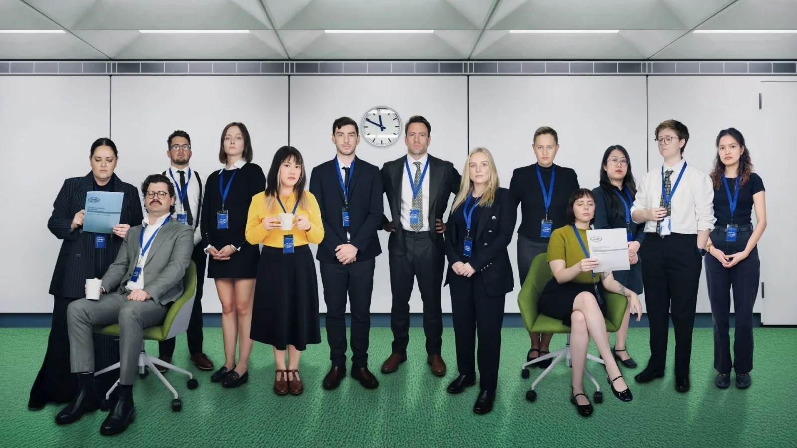 The Neighbourhood crew in corporate suits and lanyards standing in a stark office set, completely straight faced