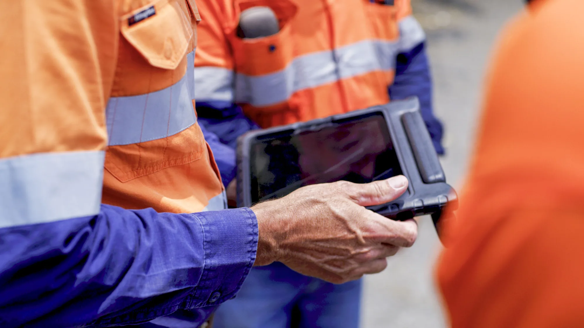 Two 3D Safety workers in orange and navy high visibility shirts, one holding a rugged tablet