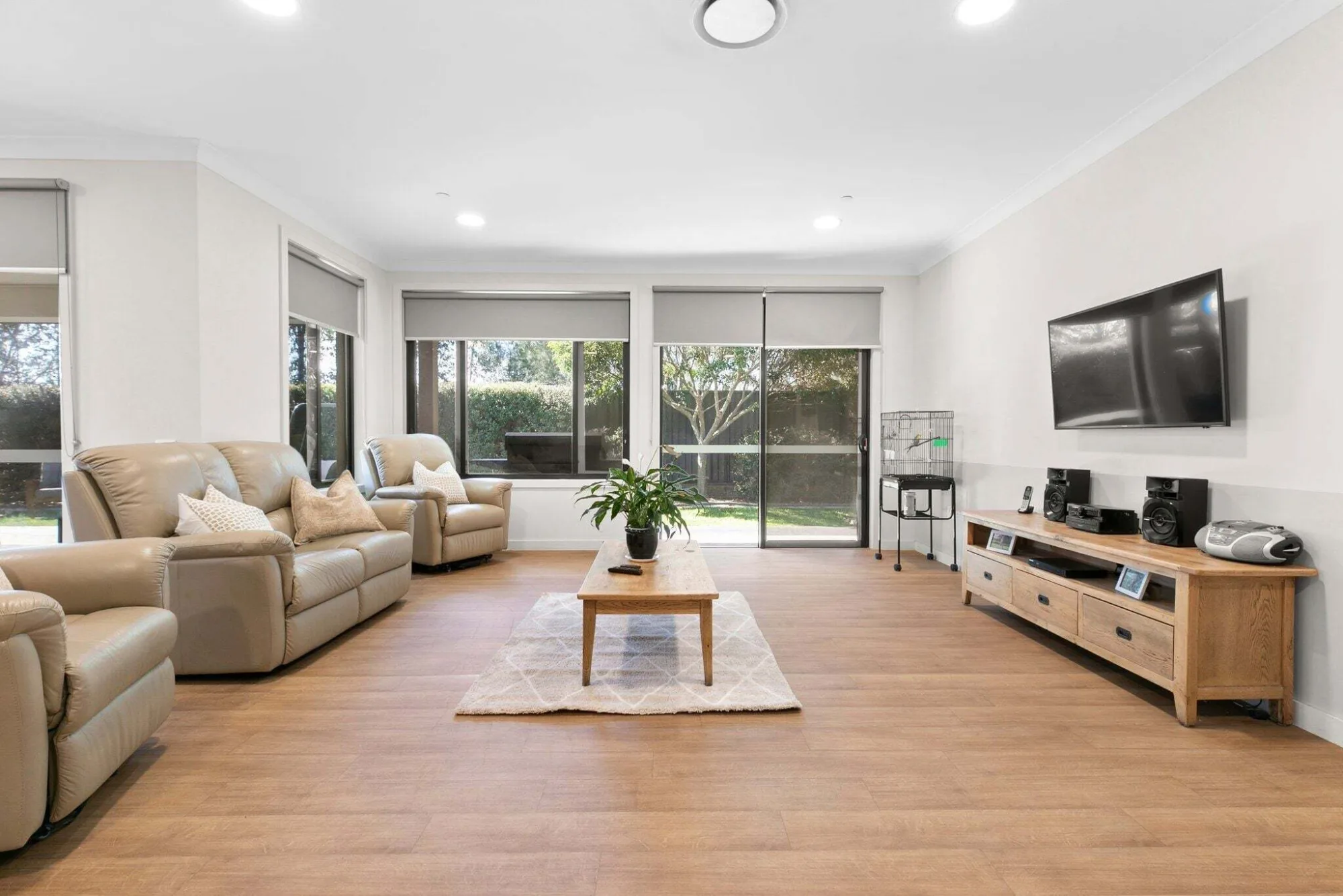 The living room of an Achieve Australia home: leather lounges, a timber coffee table and sliding doors to the garden