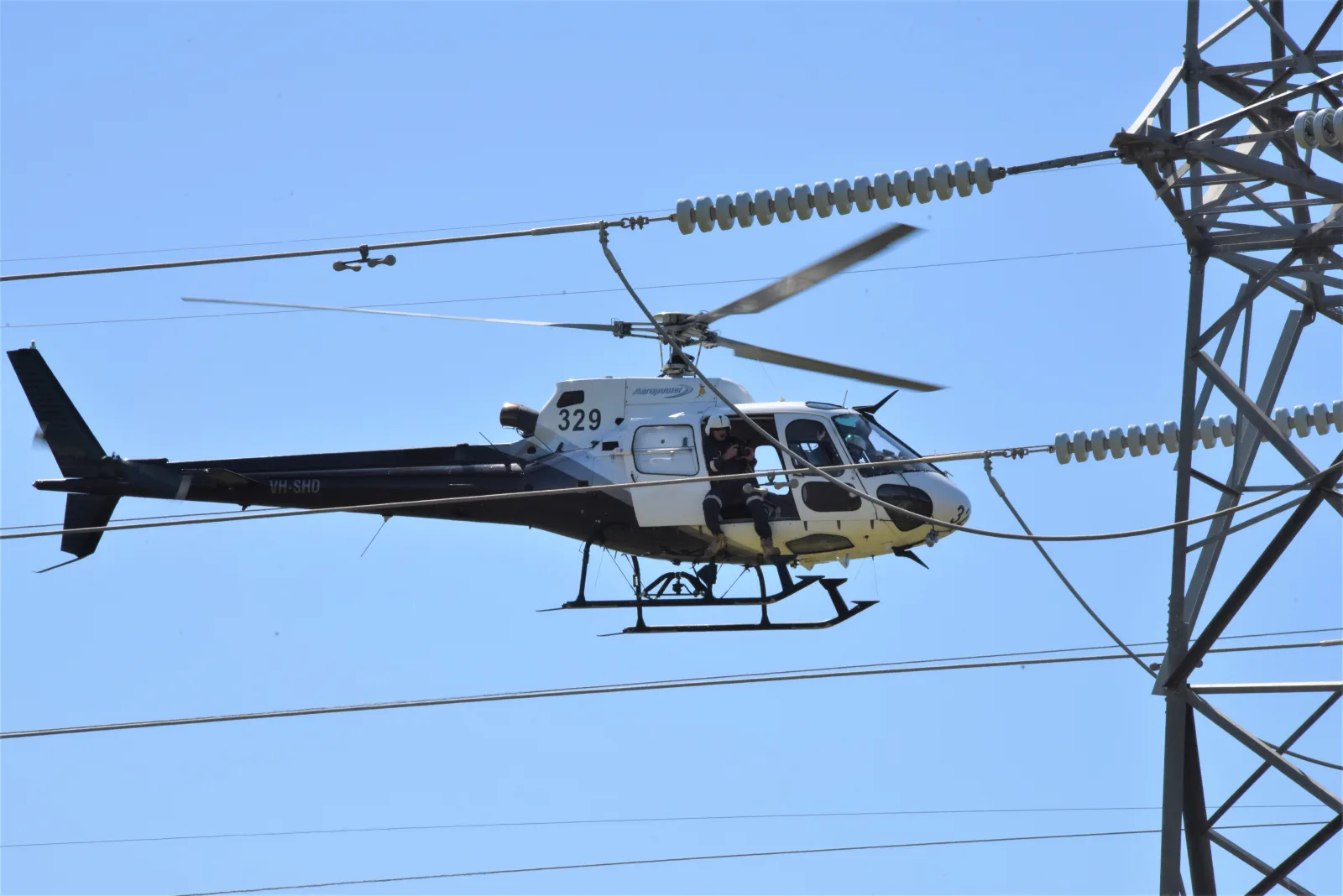 An Aeropower helicopter flying alongside high voltage power lines under a clear blue sky
