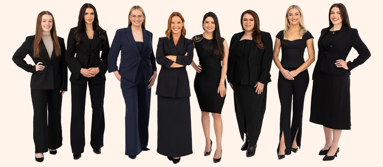 Eight women from the Flint team in dark suits and dresses, standing in a row in a studio