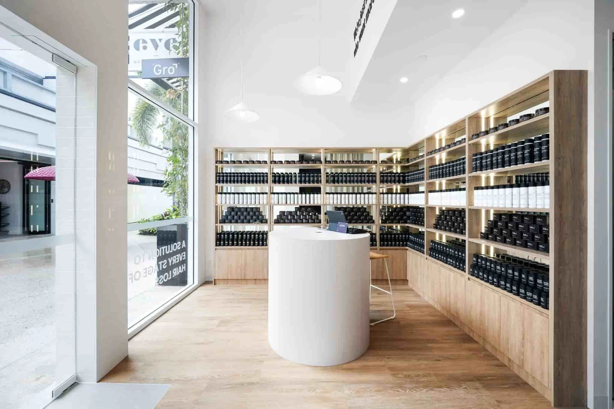 Inside a Gro Clinics clinic: timber shelving lined with black and white product bottles around a round white counter, the street through the front window