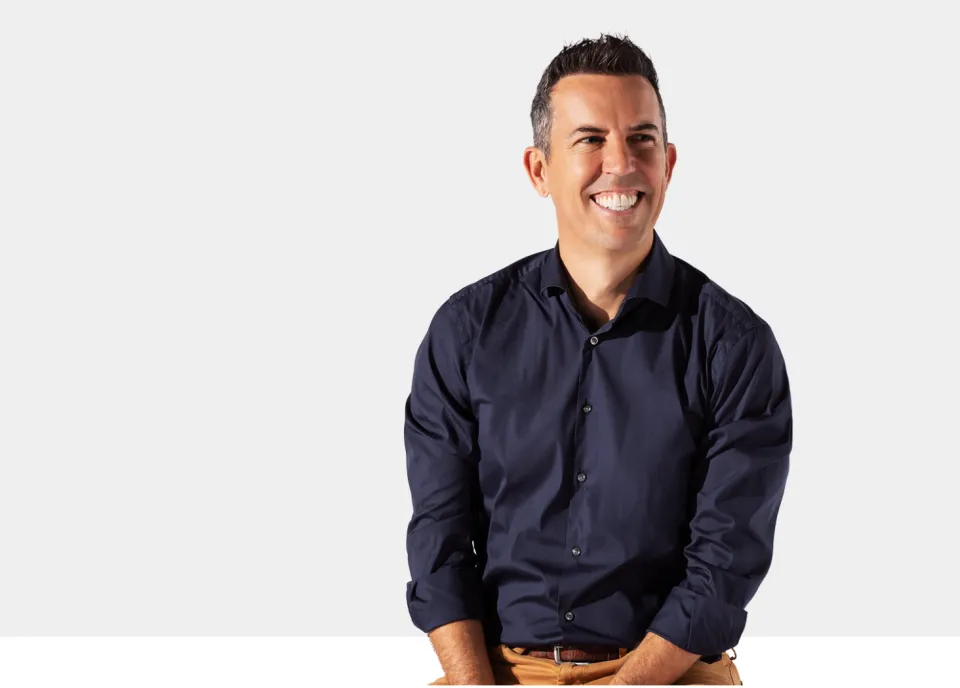 A smiling man in a navy shirt against a pale grey background