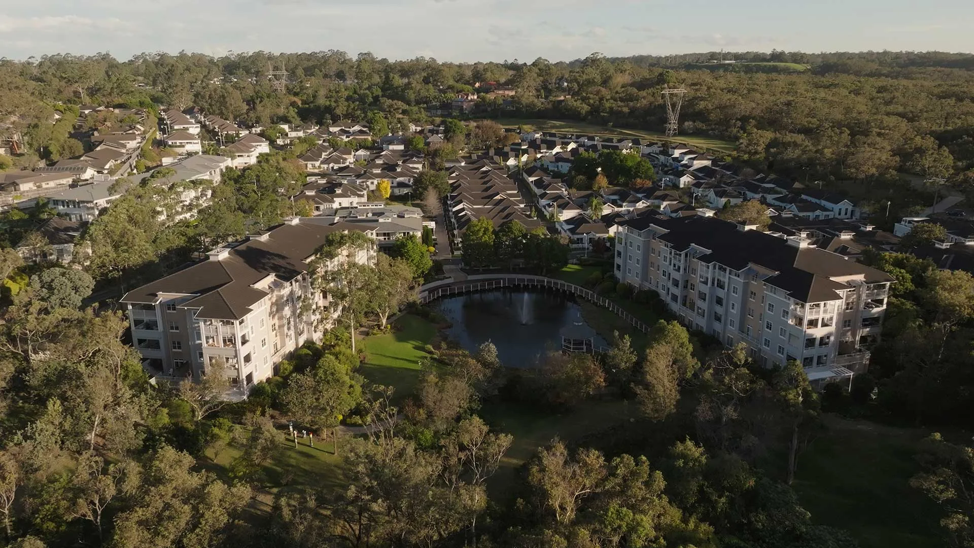 Aerial view of a seniors living village among bushland, with apartment buildings, rooftops and a small lake