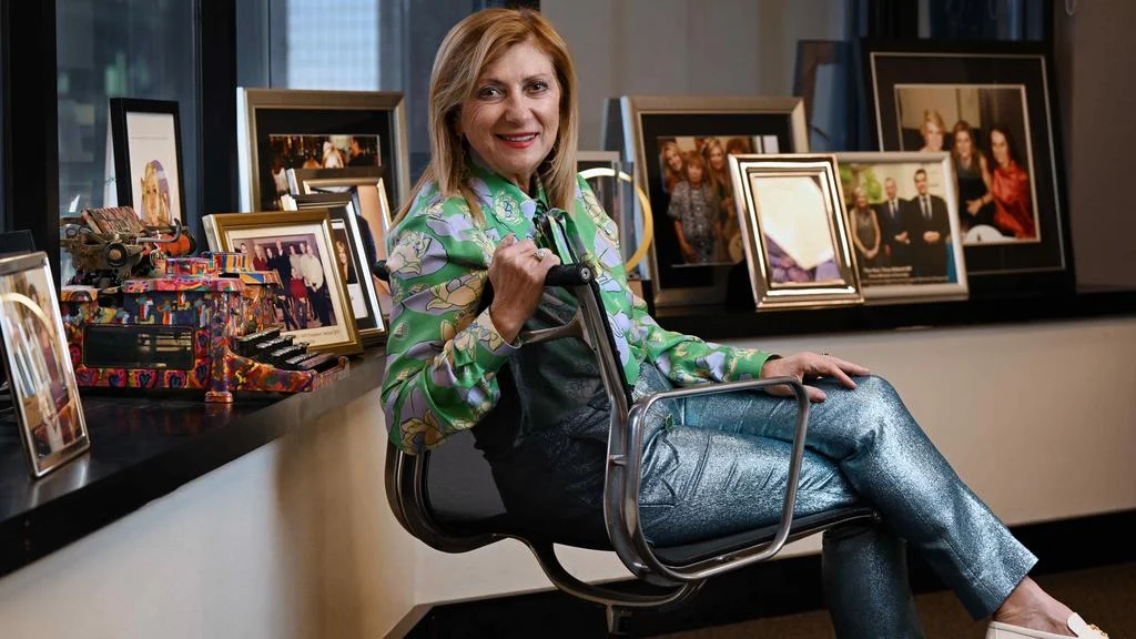 Sarina Russo seated in her office, in front of a shelf of framed photographs