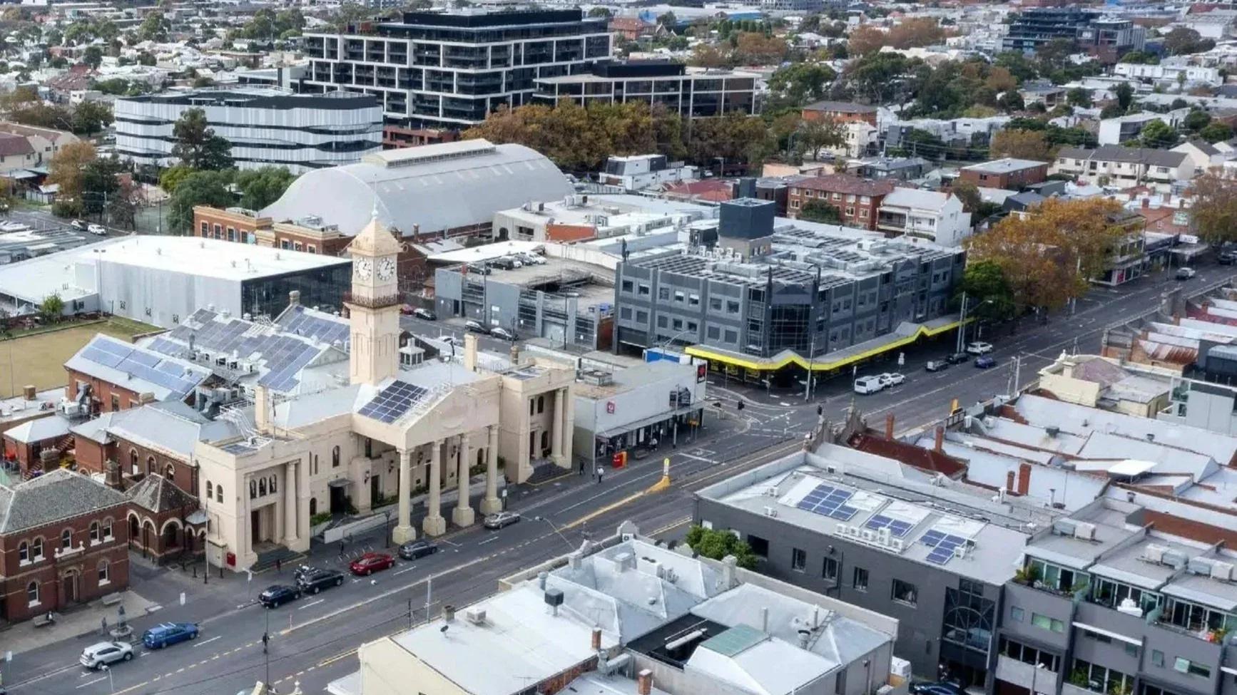 An aerial view over City of Yarra streets: a clock towered civic building with solar panels on its roof, shopfronts and houses beyond