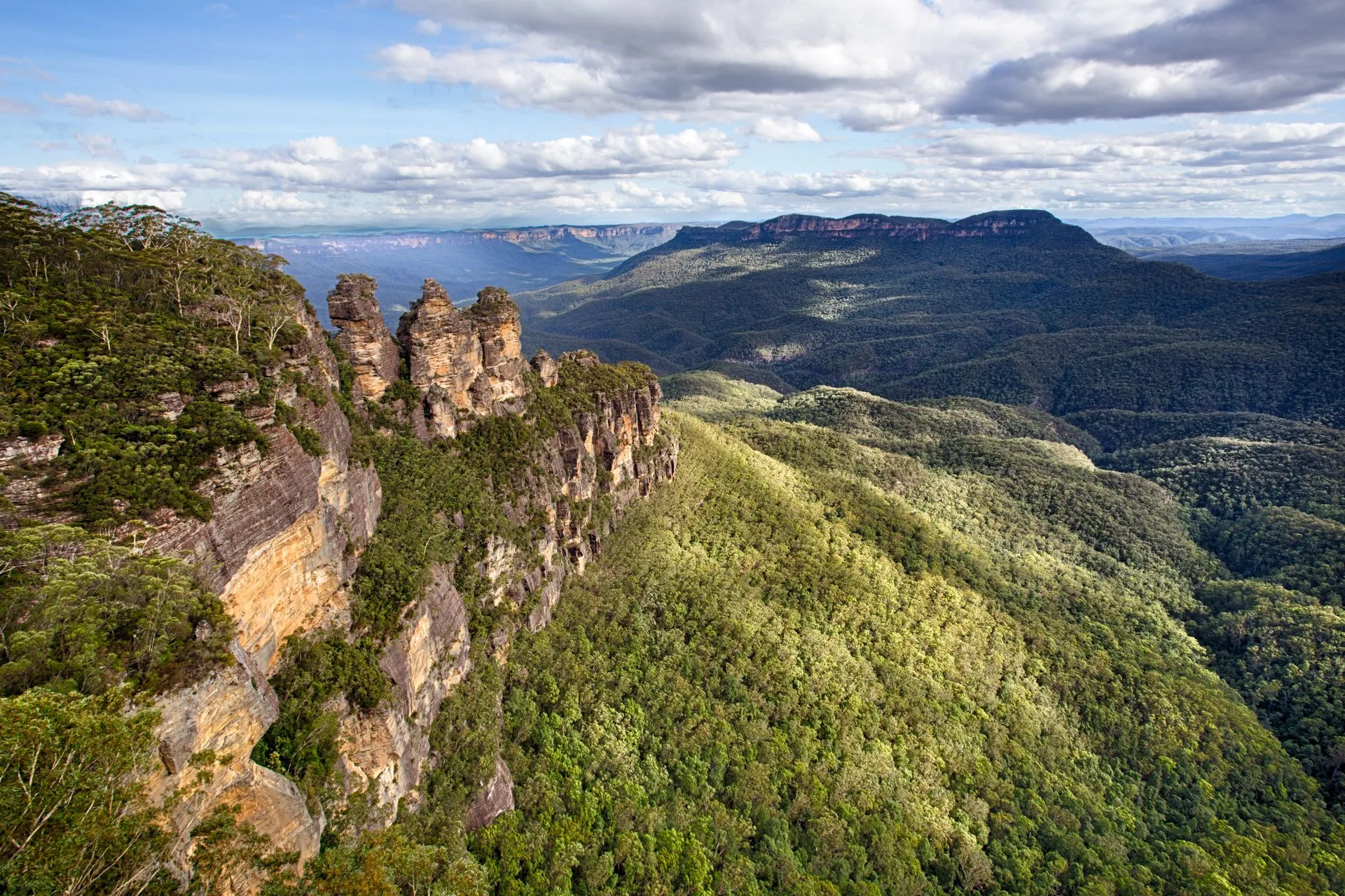 The Three Sisters in the Blue Mountains, sandstone cliffs above a forested valley under a cloudy sky