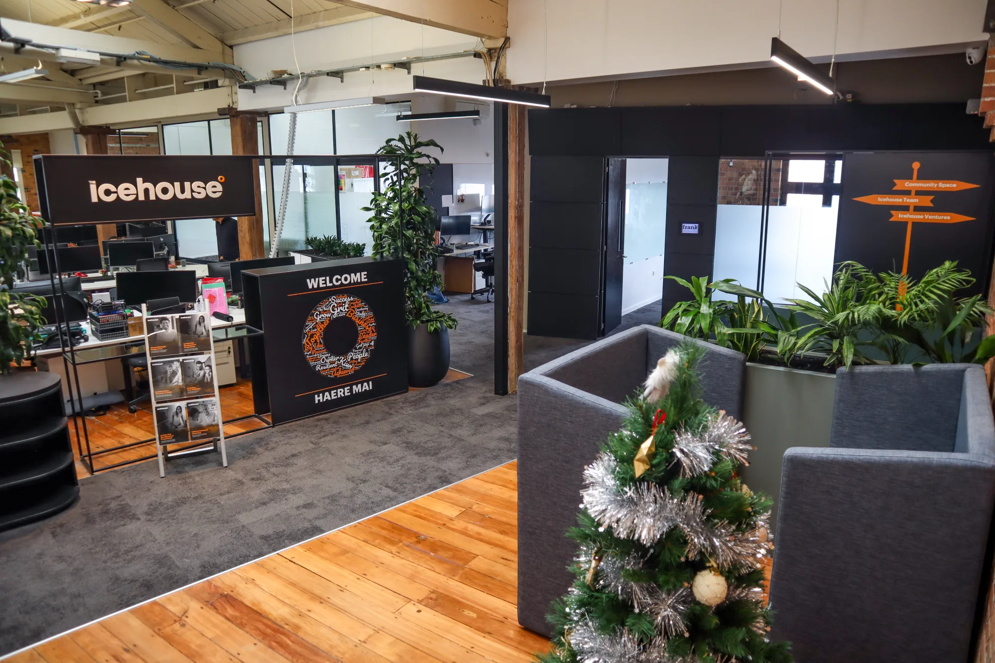 The Icehouse reception: an illuminated Icehouse sign, a welcome stand reading Haere Mai, plants and the open plan office behind
