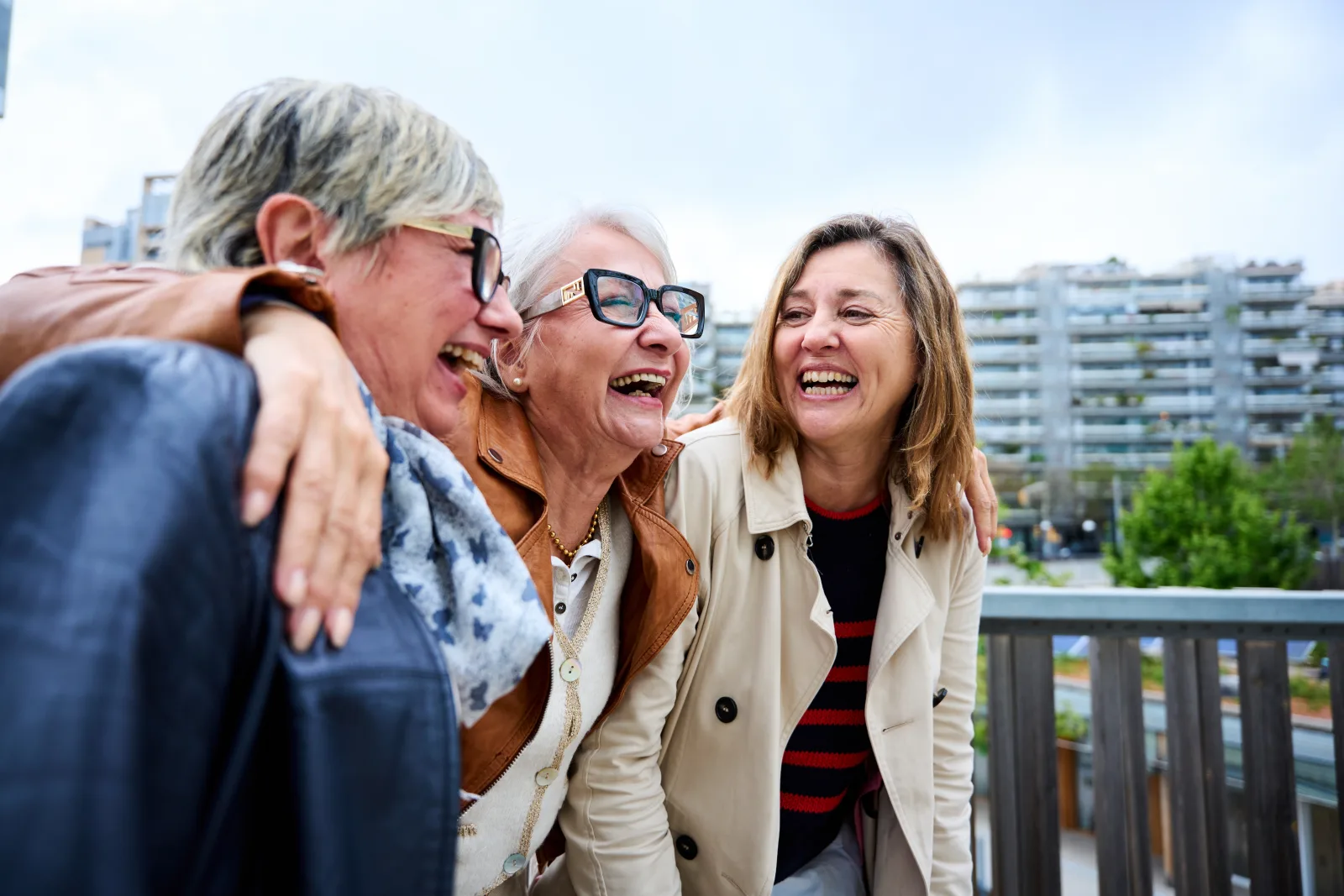 Three women laughing together with their arms around each other on a balcony
