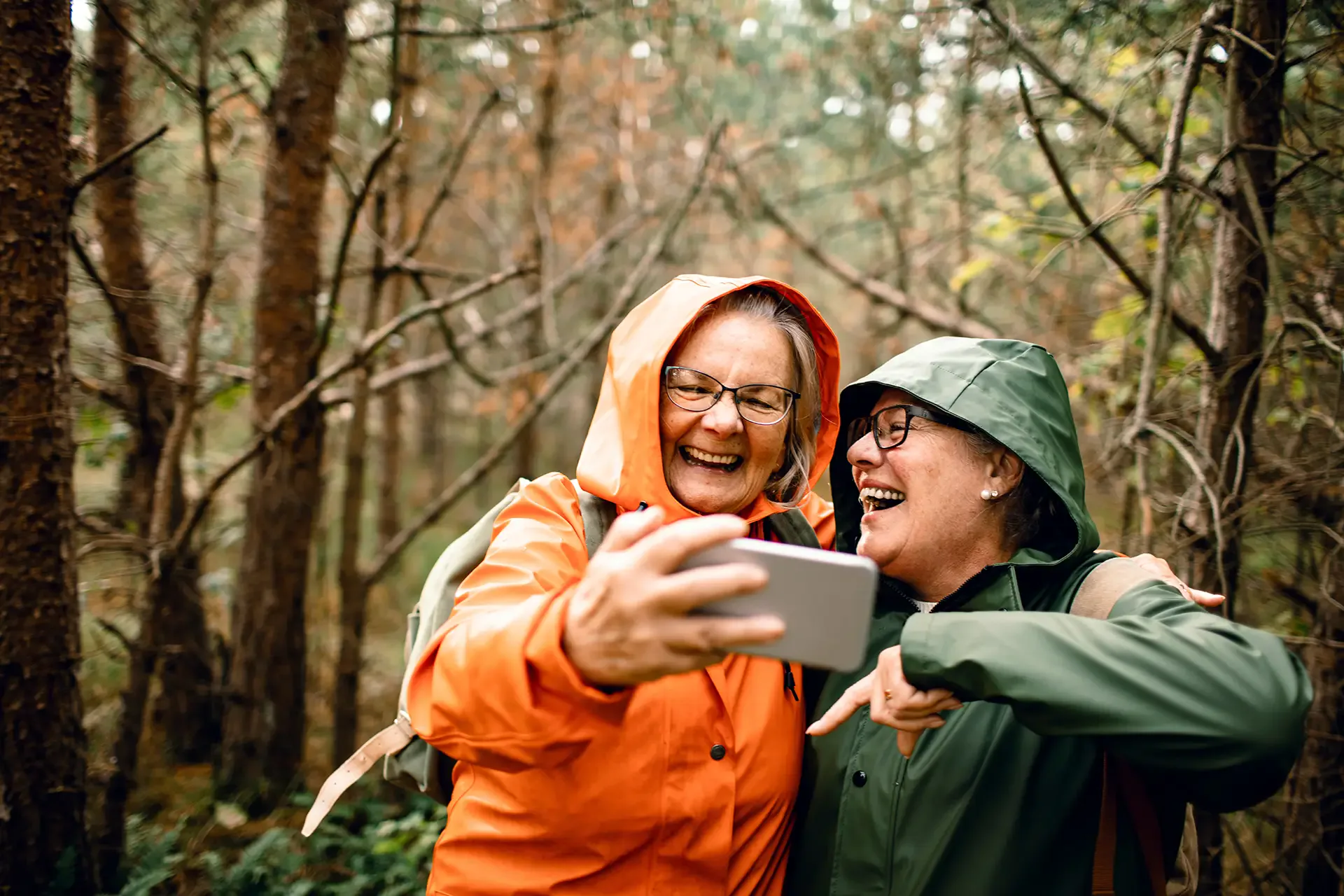 Two women in rain jackets laughing as they take a selfie on a bush walk